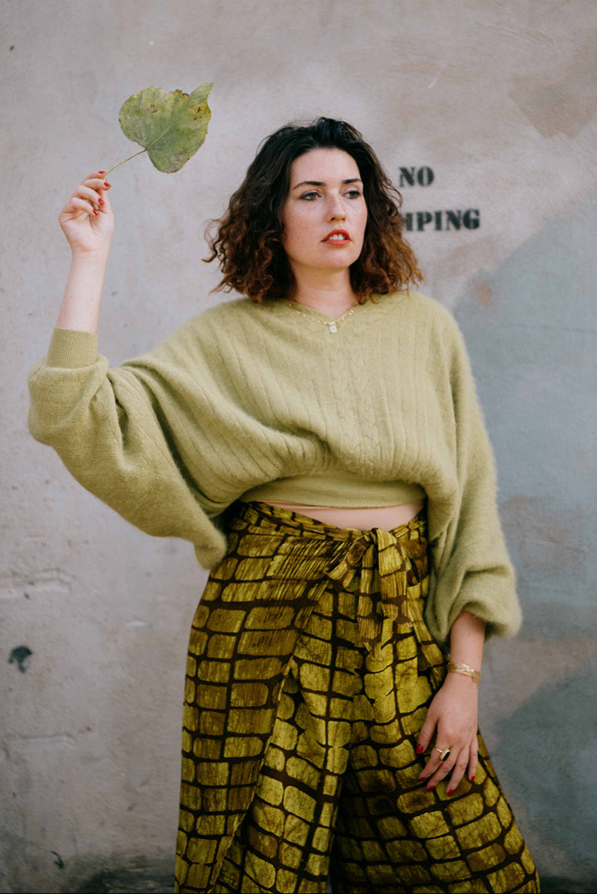 Woman holding a leaf in front of a textured wall with graffiti.