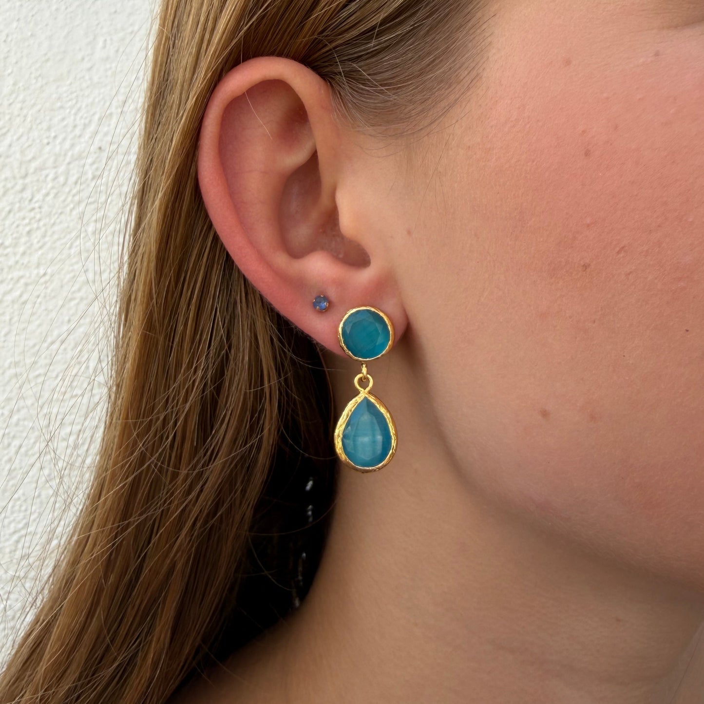 Close-up of an ear wearing a gold earring with blue gemstones.