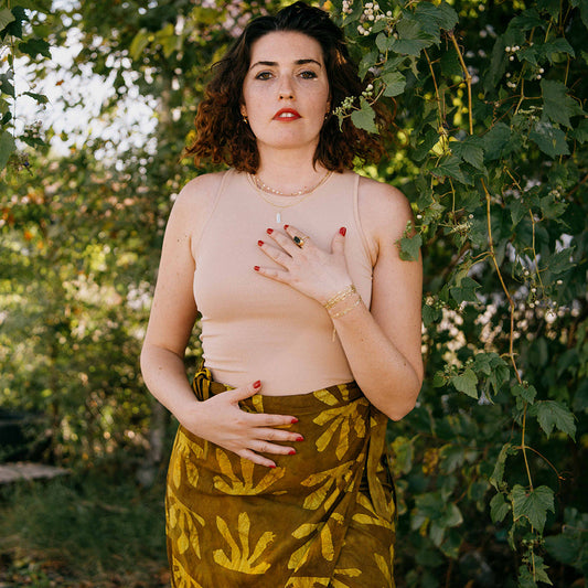 Woman wearing tan top, hand printed skirt in green and yellow